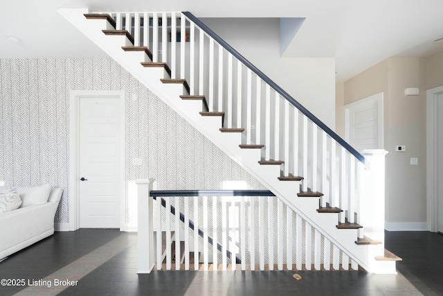 stairway with wallpapered walls, wood finished floors, baseboards, and an accent wall