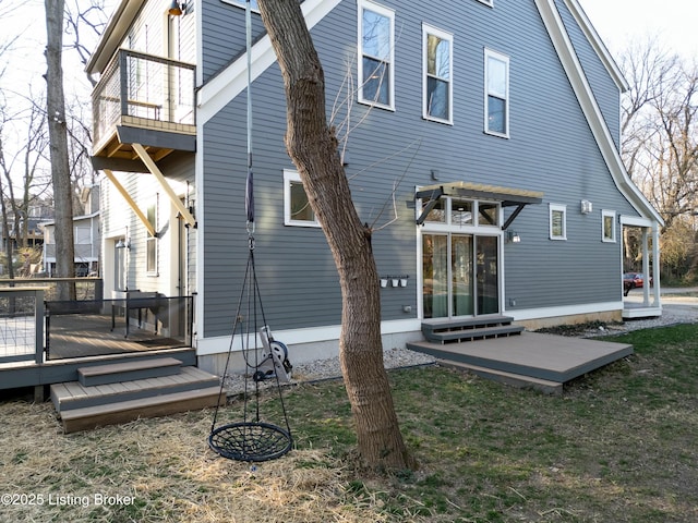 rear view of property with a deck, a lawn, and a balcony