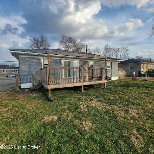 rear view of property with fence, a deck, a lawn, brick siding, and metal roof