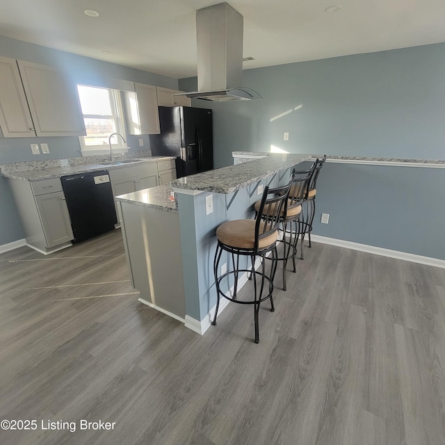 kitchen featuring a breakfast bar area, island exhaust hood, a sink, black appliances, and light wood-style floors