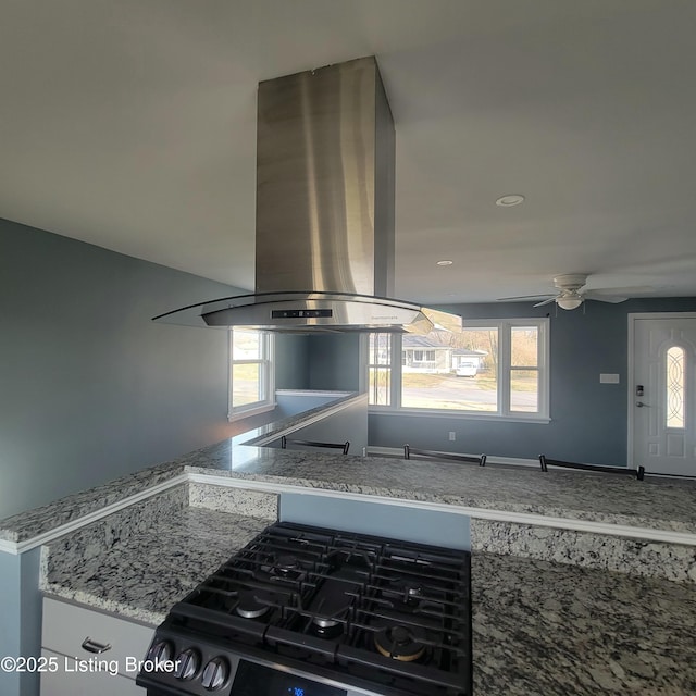 kitchen featuring black range with gas cooktop, a ceiling fan, light stone countertops, and island range hood