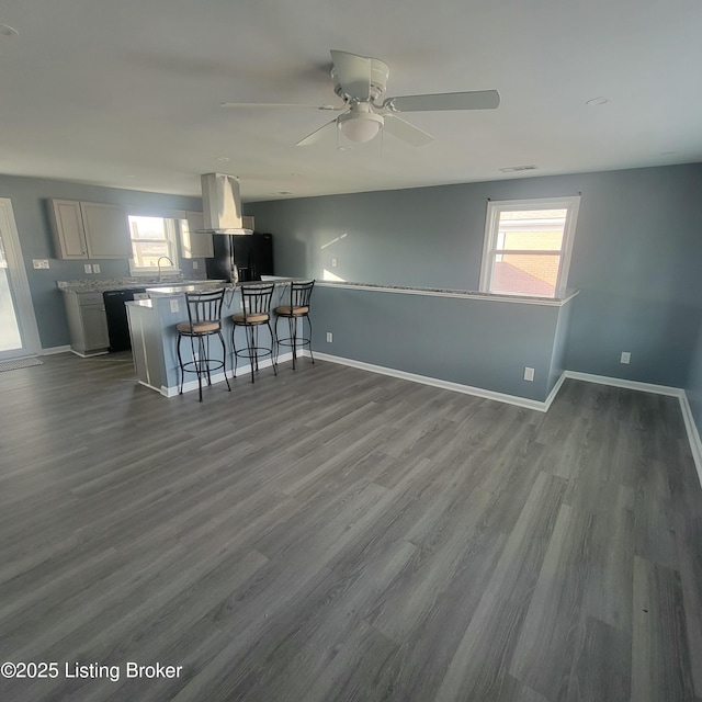 kitchen featuring baseboards, ceiling fan, black appliances, dark wood-type flooring, and a kitchen bar