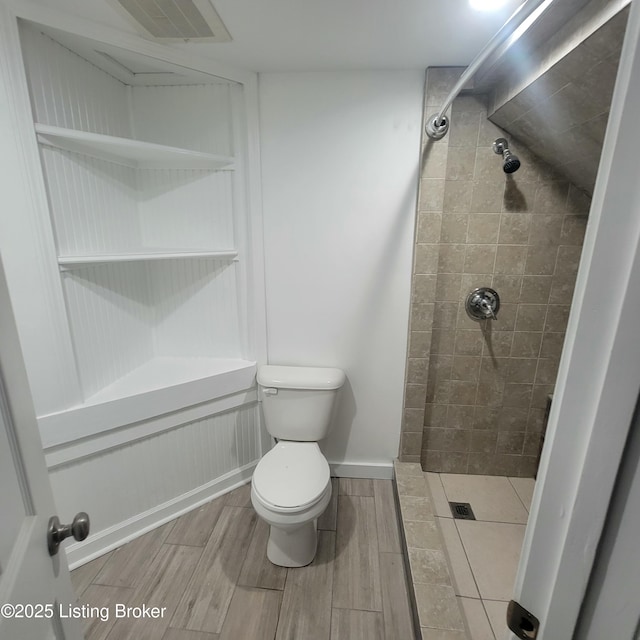 bathroom featuring visible vents, baseboards, wood finish floors, toilet, and tiled shower