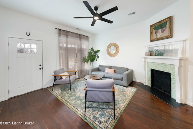 living room featuring visible vents, a ceiling fan, wood-type flooring, a stone fireplace, and baseboards