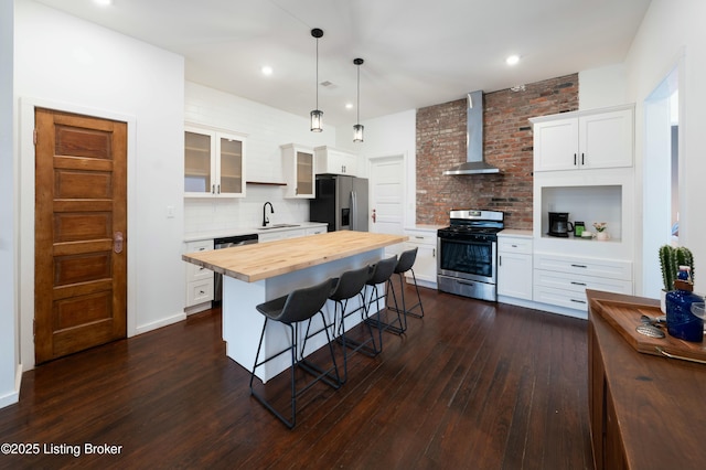 kitchen featuring wooden counters, a breakfast bar, a sink, stainless steel appliances, and wall chimney exhaust hood