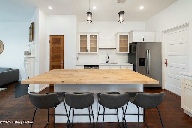 kitchen with butcher block countertops, a sink, a kitchen island, appliances with stainless steel finishes, and glass insert cabinets