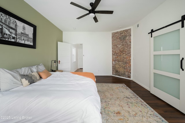 bedroom with visible vents, wood finished floors, a barn door, baseboards, and ceiling fan