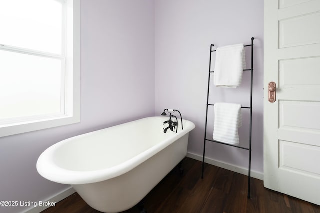 bathroom featuring baseboards, a freestanding bath, and wood finished floors