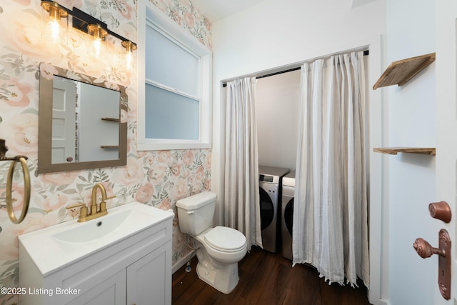 bathroom with washing machine and clothes dryer, wallpapered walls, toilet, wood finished floors, and vanity