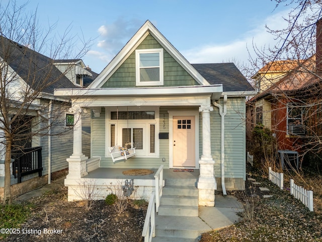 view of front facade with covered porch, a shingled roof, and fence