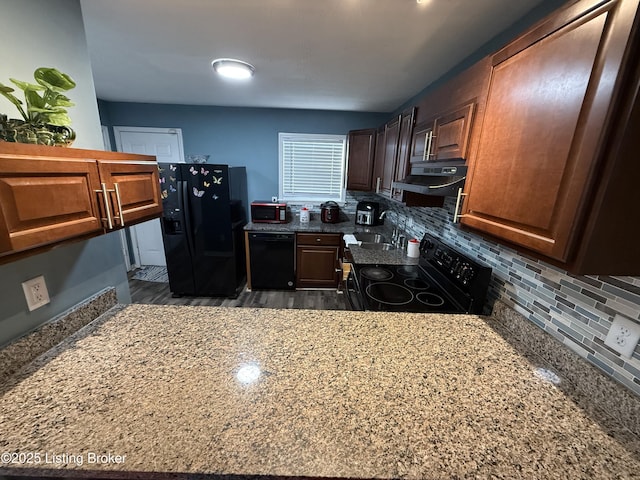 kitchen featuring black appliances, under cabinet range hood, a sink, stone counters, and decorative backsplash