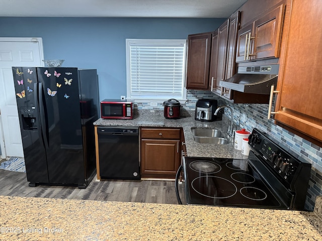 kitchen with light wood-type flooring, black appliances, a sink, under cabinet range hood, and backsplash