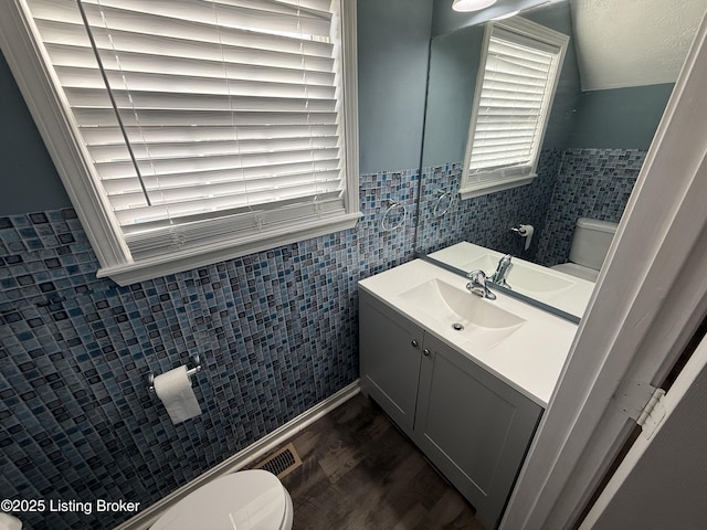 bathroom with vanity, wood finished floors, lofted ceiling, tile walls, and toilet