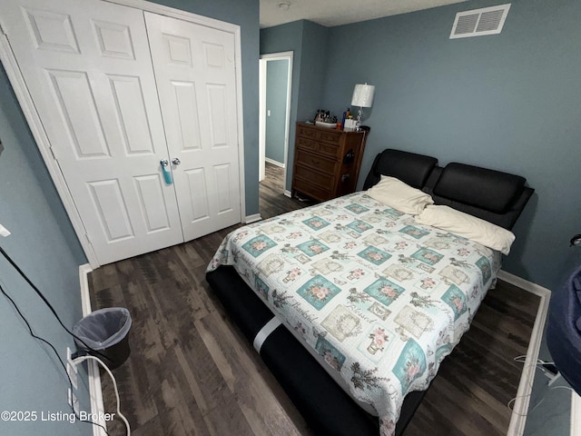 bedroom with a closet, visible vents, dark wood-type flooring, and baseboards