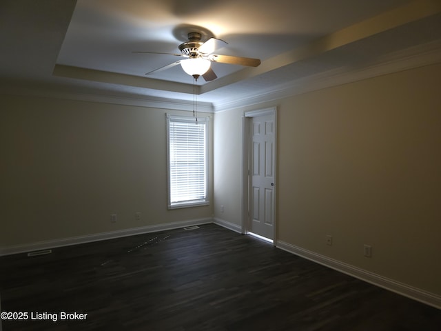 empty room with a raised ceiling, dark wood-type flooring, a ceiling fan, crown molding, and baseboards