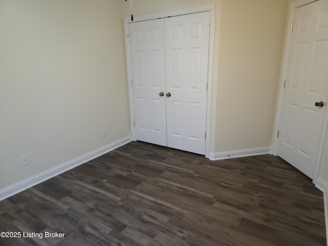 unfurnished bedroom featuring a closet, baseboards, and dark wood-style floors