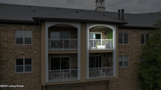 back of property with brick siding, a balcony, and a shingled roof