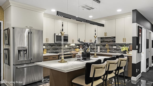 kitchen featuring visible vents, stainless steel appliances, decorative light fixtures, backsplash, and a center island