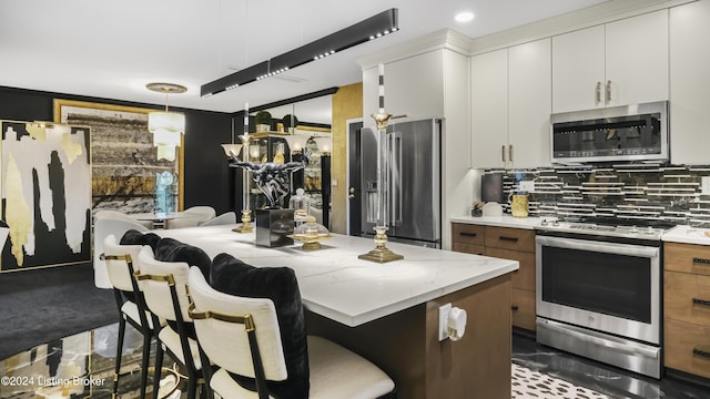 kitchen featuring brown cabinetry, stainless steel appliances, white cabinets, a kitchen bar, and tasteful backsplash