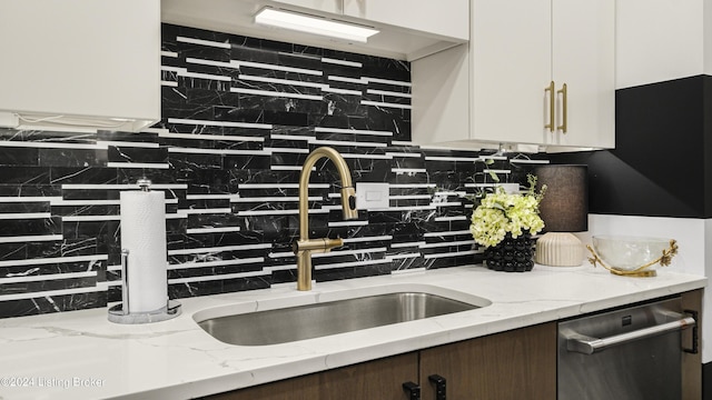 kitchen with tasteful backsplash, dishwasher, light stone counters, white cabinets, and a sink