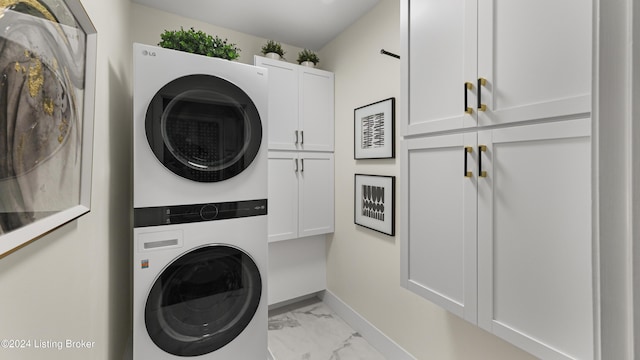 laundry area featuring cabinet space, stacked washer and clothes dryer, marble finish floor, and baseboards