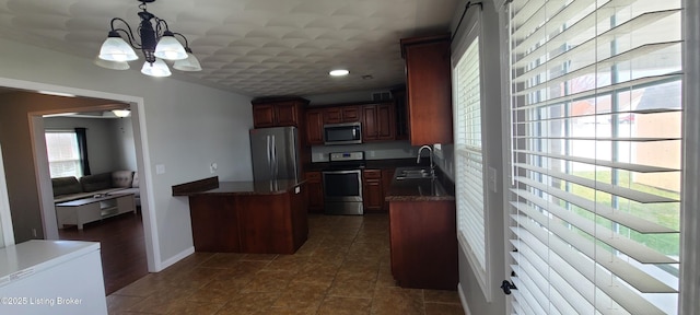 kitchen featuring appliances with stainless steel finishes, a peninsula, an inviting chandelier, hanging light fixtures, and a sink