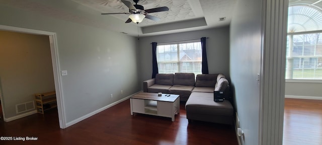 living area with a healthy amount of sunlight, baseboards, a tray ceiling, and wood finished floors