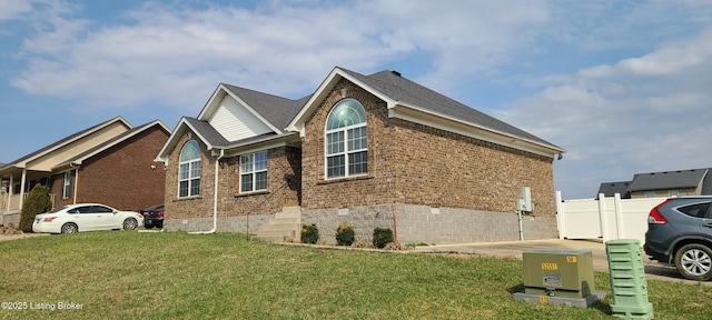 view of home's exterior with brick siding, a lawn, roof with shingles, and fence