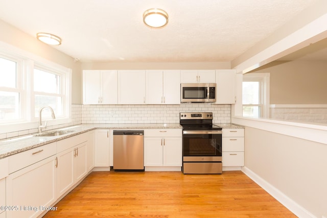 kitchen with light wood finished floors, stainless steel appliances, tasteful backsplash, and a sink