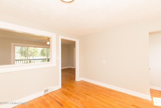 empty room with visible vents, baseboards, ceiling fan, light wood-type flooring, and a textured ceiling