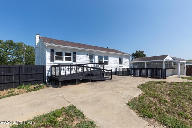 rear view of house with a wooden deck, stone siding, a chimney, and fence