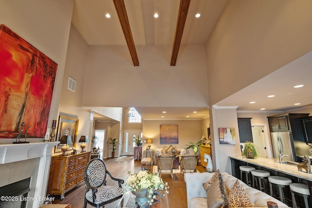 living area featuring visible vents, beamed ceiling, a high ceiling, and wood finished floors