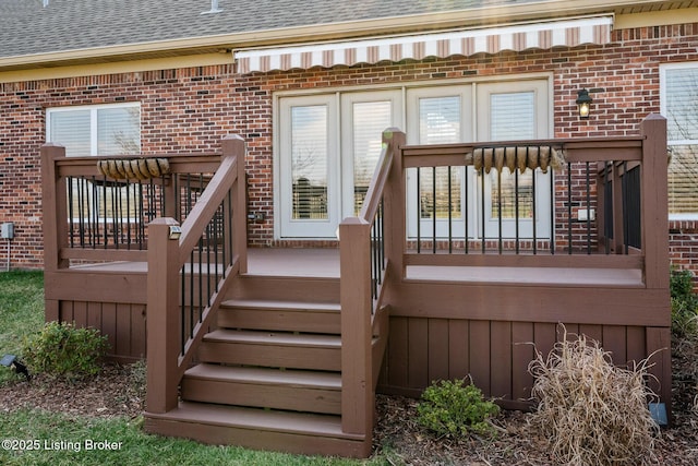 entrance to property featuring a deck, brick siding, and roof with shingles