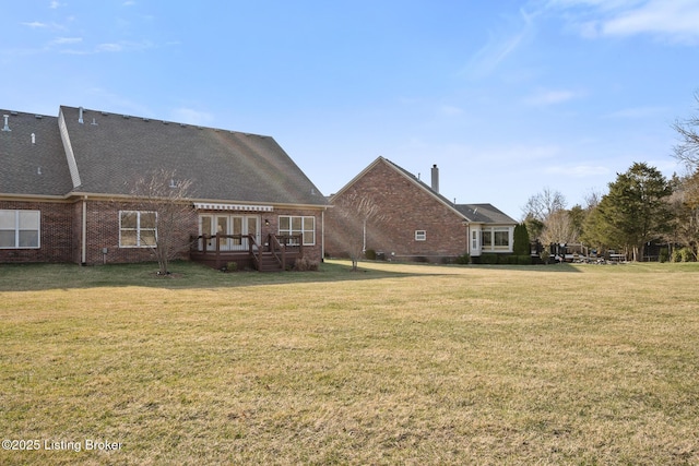 rear view of property featuring brick siding, roof with shingles, and a lawn