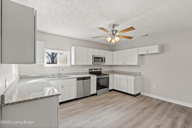 kitchen with light stone counters, visible vents, a sink, stainless steel appliances, and light wood-type flooring