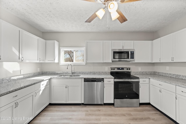 kitchen with light wood-style flooring, a ceiling fan, a sink, white cabinetry, and stainless steel appliances