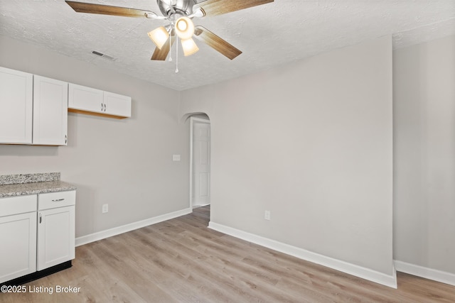 kitchen featuring baseboards, visible vents, arched walkways, white cabinets, and light wood-type flooring