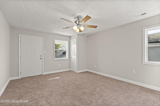 carpeted empty room with visible vents, a textured ceiling, baseboards, and a ceiling fan