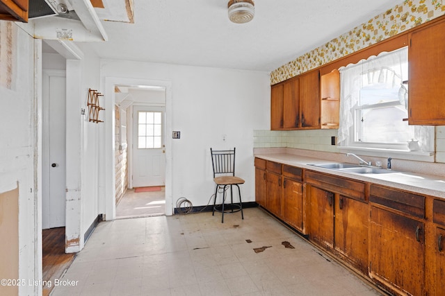 kitchen featuring a sink, backsplash, brown cabinetry, light countertops, and light floors