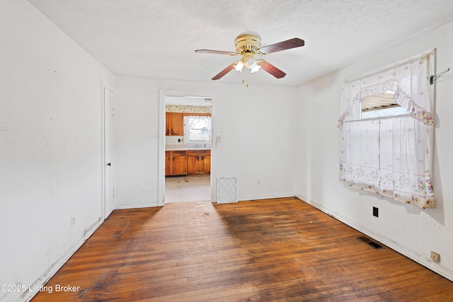 unfurnished room featuring a textured ceiling, hardwood / wood-style flooring, visible vents, and ceiling fan