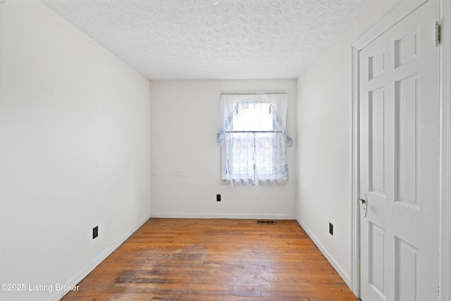 unfurnished bedroom with hardwood / wood-style flooring, visible vents, baseboards, and a textured ceiling