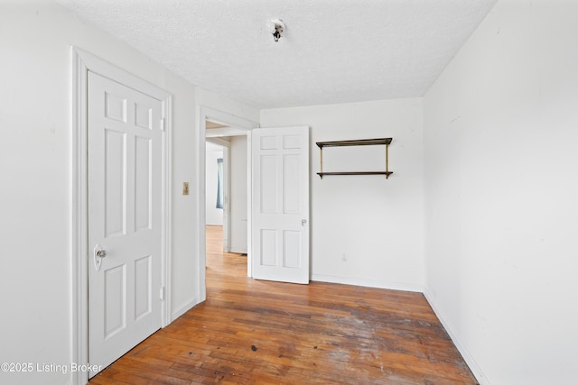 unfurnished bedroom with a textured ceiling, baseboards, and hardwood / wood-style floors