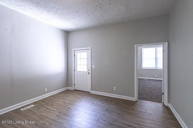 unfurnished room with visible vents, a textured ceiling, baseboards, and wood finished floors