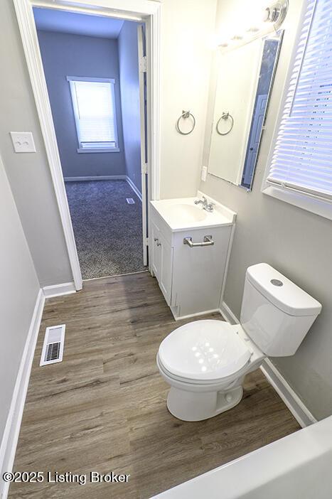 half bath with visible vents, baseboards, toilet, wood finished floors, and vanity