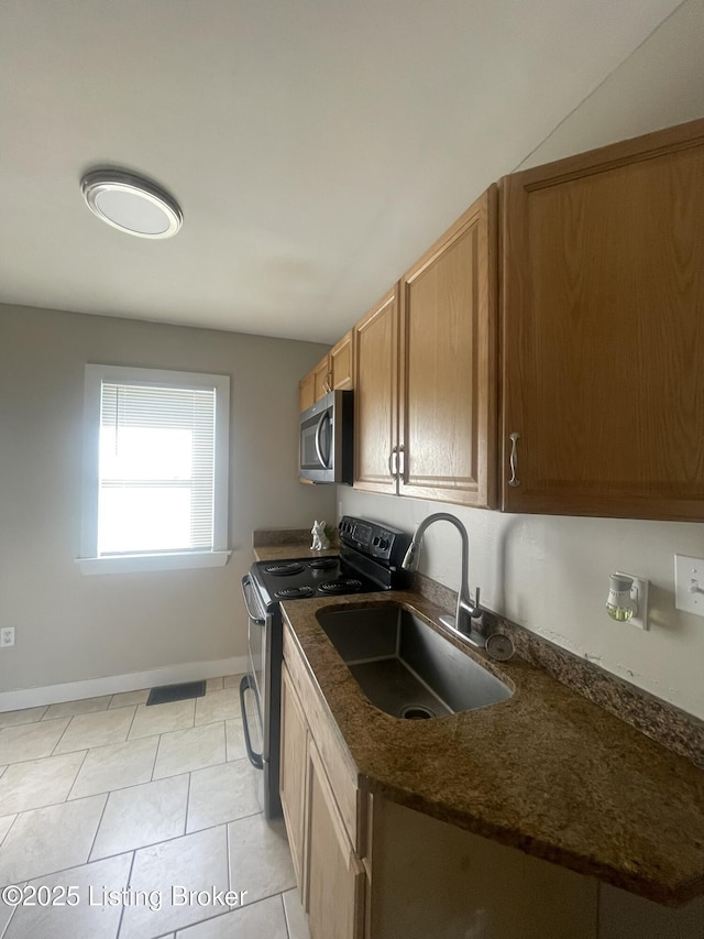 kitchen featuring light tile patterned floors, baseboards, dark stone counters, a sink, and appliances with stainless steel finishes