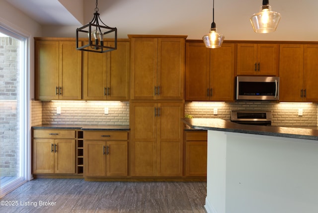 kitchen with an inviting chandelier, stainless steel microwave, dark countertops, and brown cabinetry