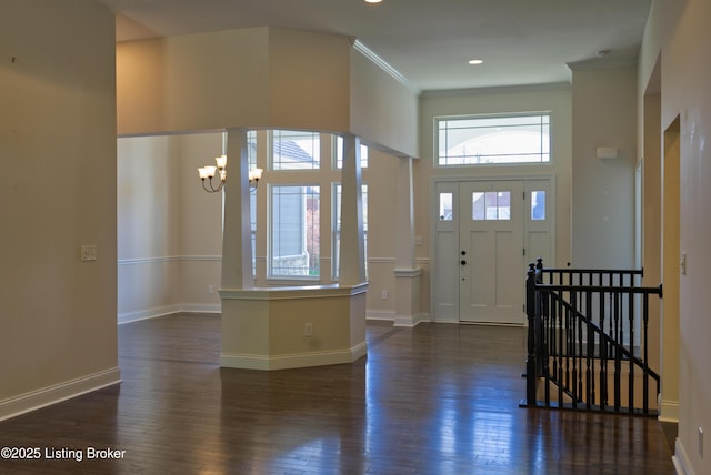 entryway featuring baseboards, ornamental molding, dark wood finished floors, a notable chandelier, and a high ceiling