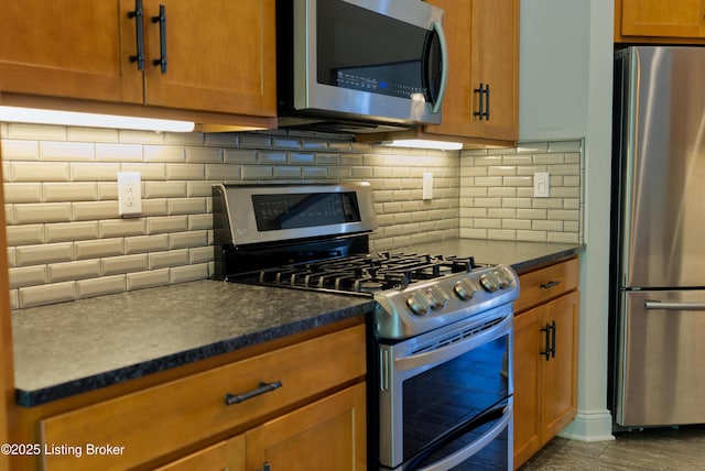 kitchen featuring dark countertops, brown cabinets, appliances with stainless steel finishes, and decorative backsplash