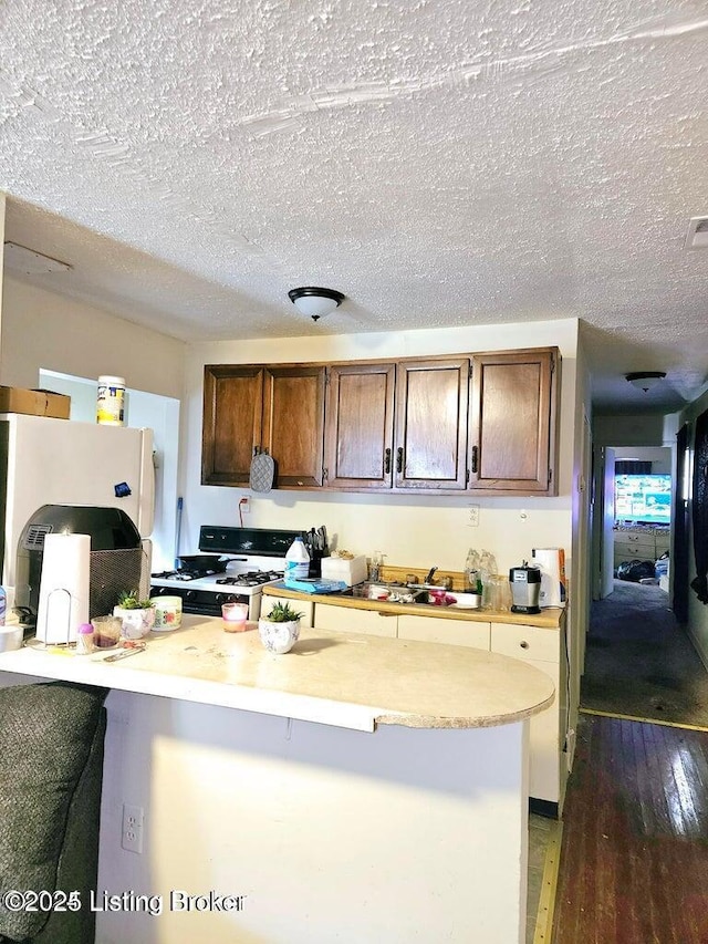 kitchen featuring wood finished floors, gas stove, white fridge, light countertops, and a textured ceiling