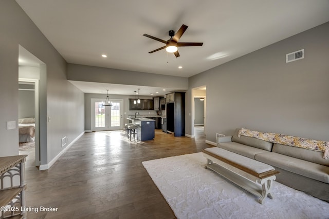 living area featuring visible vents, baseboards, wood finished floors, and ceiling fan with notable chandelier